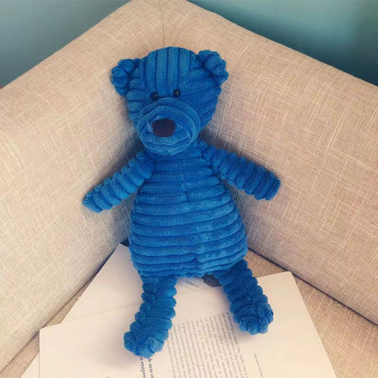 Blue teddy bear plush toy on a beige couch with a book underneath